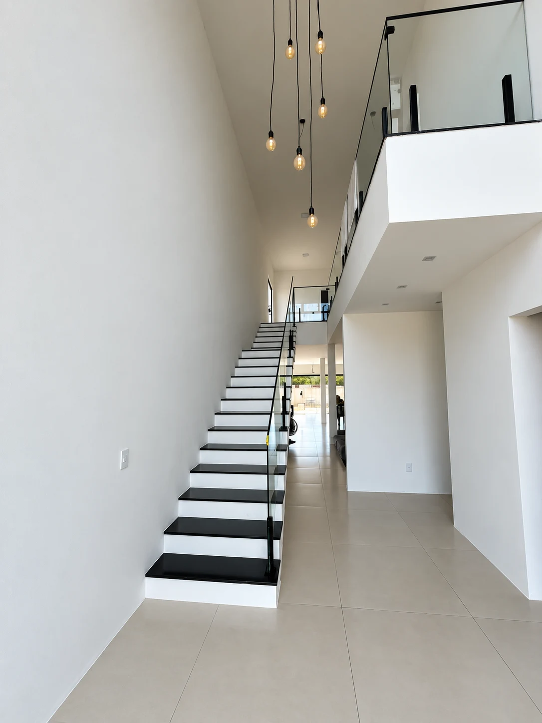 Escada com degraus pretos, guarda-corpo de vidro e pé-direito alto
